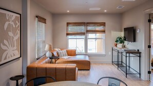 A modern living room with a sofa, a dining table, and a TV. - Gloria Inn Unit 3- 5 minutes from Baylor and 2 Blocks to Magnolia (Waco)