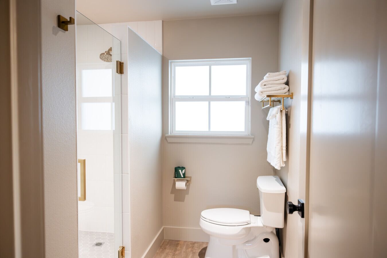 A bathroom with a toilet, a window, a towel rack, and a shower area.