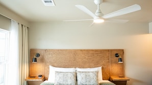 Une chambre à coucher avec un lit, un ventilateur de plafond, des lampes de chevet et une fenêtre.