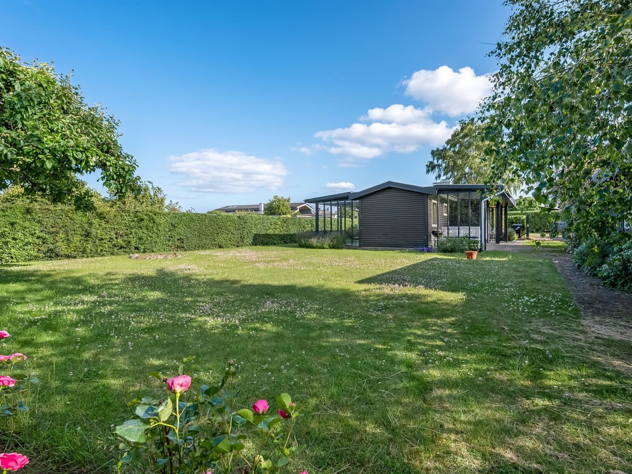 A modern house with a large glass conservatory, surrounded by a well-maintained lawn and flowering plants.