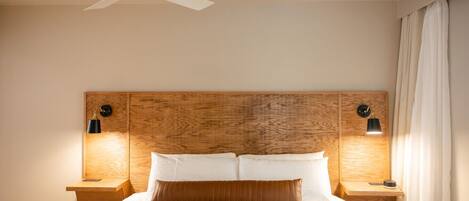 Une chambre à coucher avec une tête de lit en bois, deux lampes de chevet, un ventilateur de plafond et un lit recouvert d’une couette verte.