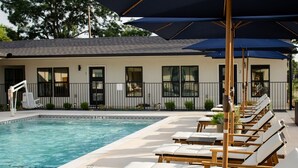 A poolside area with lounge chairs and umbrellas, a pool, and a building with windows and a fence in the background. - Gloria Inn Unit 5 -5 minutes from Baylor and 2 Blocks to Magnolia (Waco)