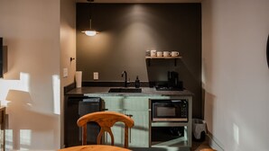 Ett litet, praktiskt kök med en diskho, en kaffebryggare, en mikrovågsugn och en hylla med koppar.