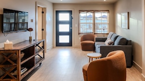 Una sala moderna con sofá, sillón, televisor y una mesa de madera.