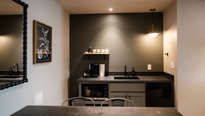 Una cocina compacta con cafetera, un lavamanos y microondas. Hay una mesa de comedor con sillas y un cuadro en la pared.
