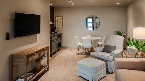Un salon moderne doté d’un téléviseur à écran plat, d’un coin repas avec une table ronde et des chaises, d’un canapé et d’un petit pouf.