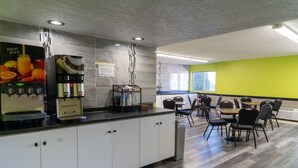 Una cocina moderna con dispensador de jugo de frutas, máquina de café y zona de comedor con mesas y sillas.