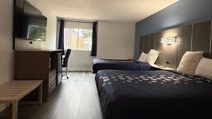 Habitación de hotel con dos camas, un escritorio, una silla, un televisor y una ventana con cortinas.