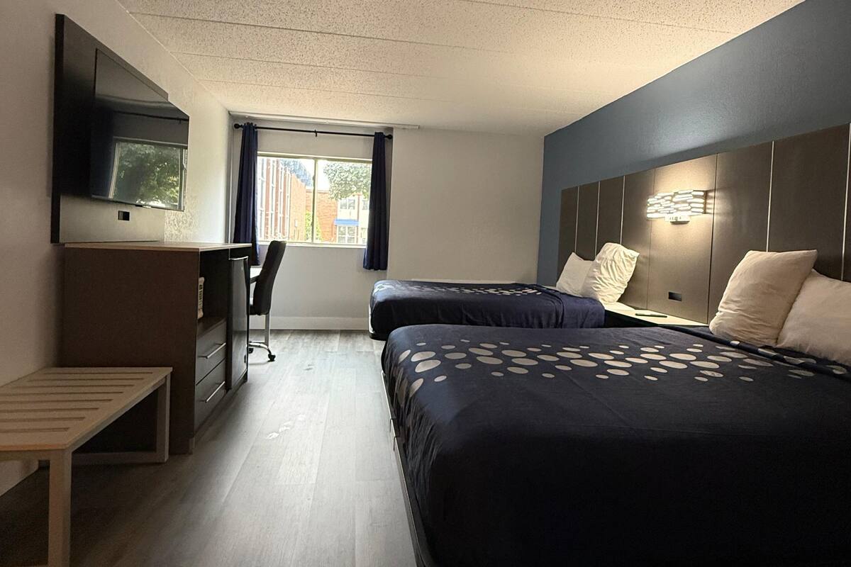 A hotel room with two beds, a desk, a chair, a TV, and a window with curtains.