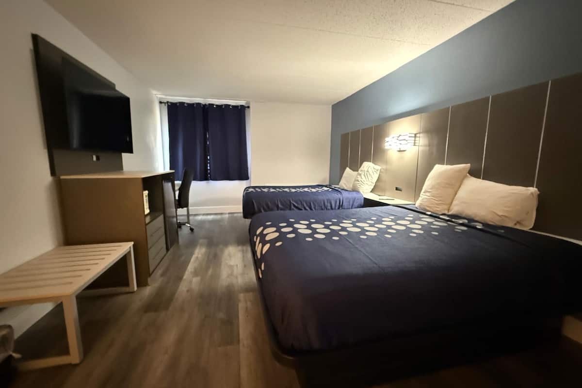 A hotel room with two beds, a TV, a desk, and a window with curtains.