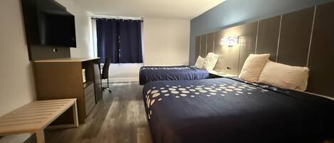 Habitación de hotel con dos camas, televisor, escritorio y ventana con cortinas.