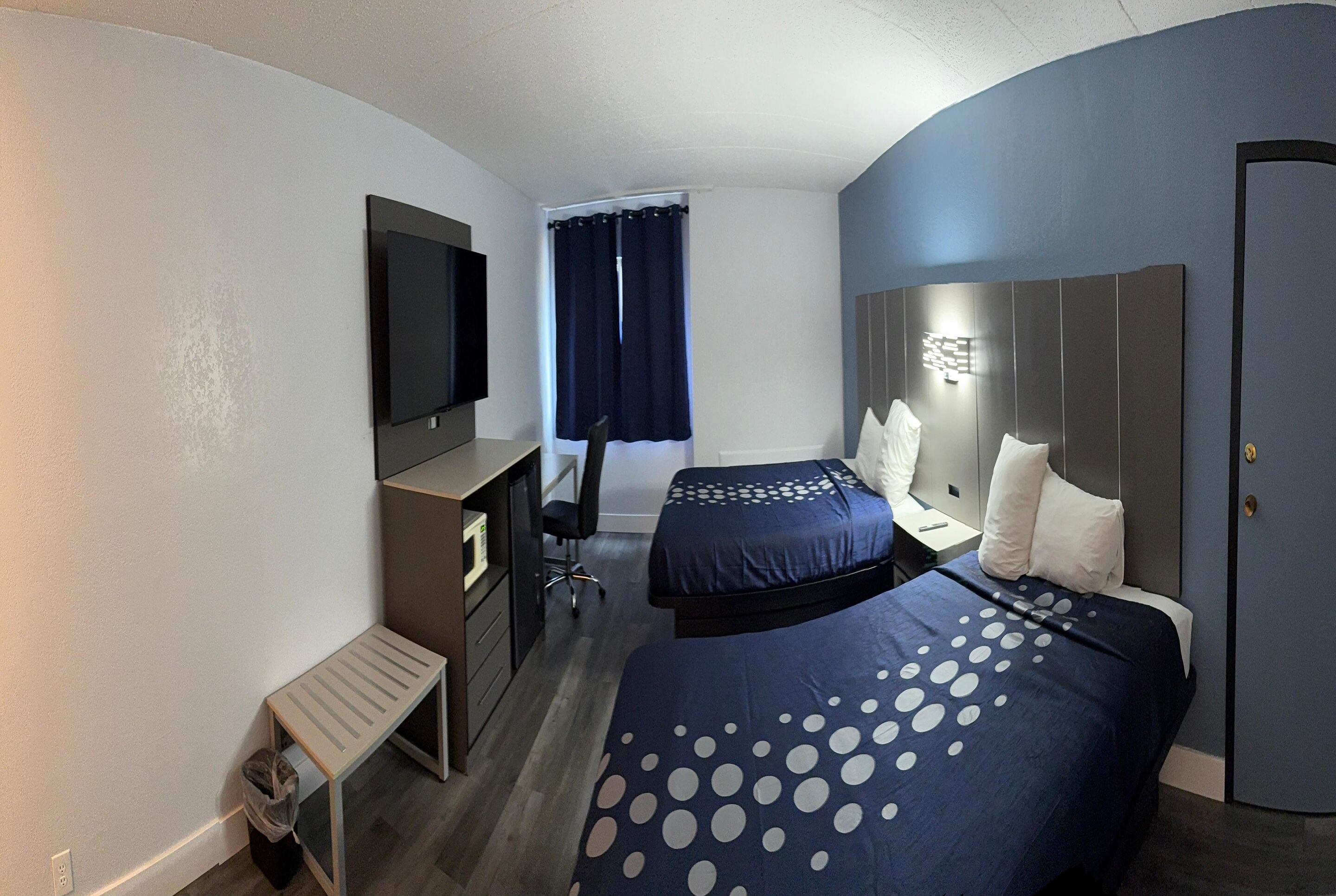 A hotel room with two beds, a desk, a TV, and a window with curtains.