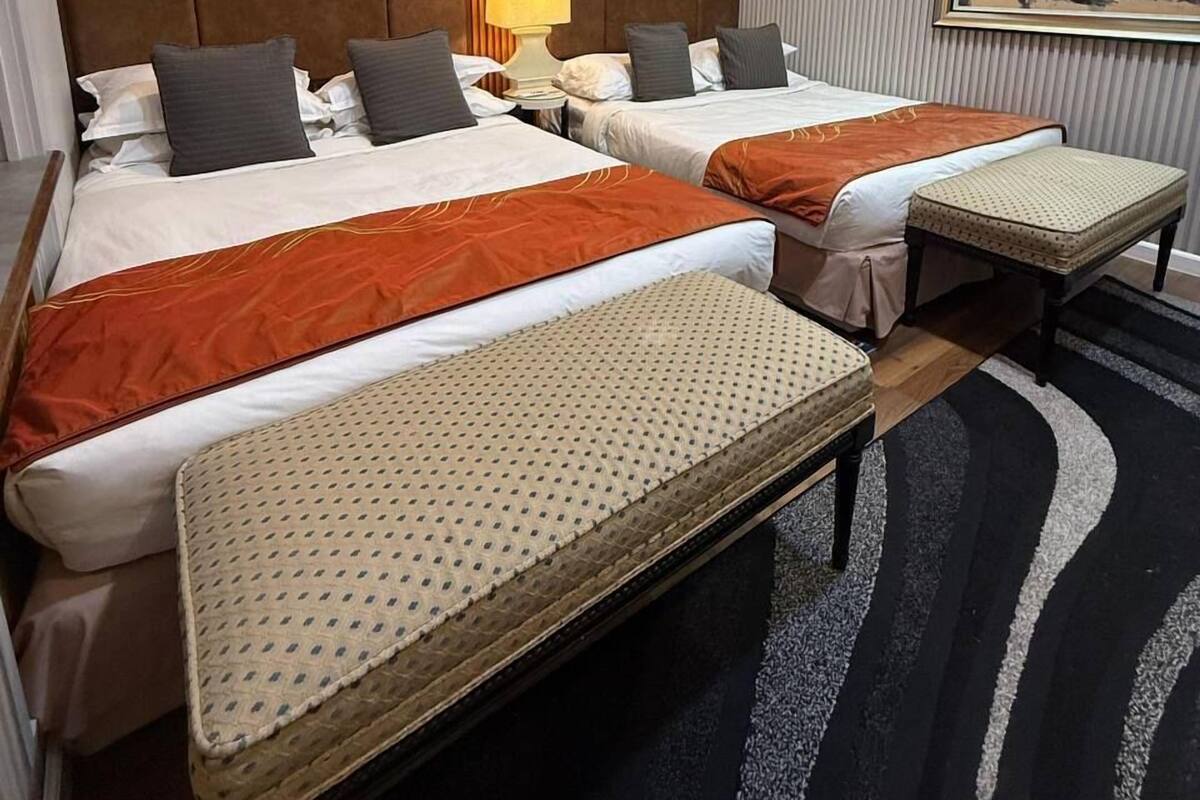 Ein Hotelzimmer mit zwei Betten, einer schrägen Holzbalkendecke, einer Klimaanlage, einem Nachttisch mit Lampe und einem Bild an der Wand.