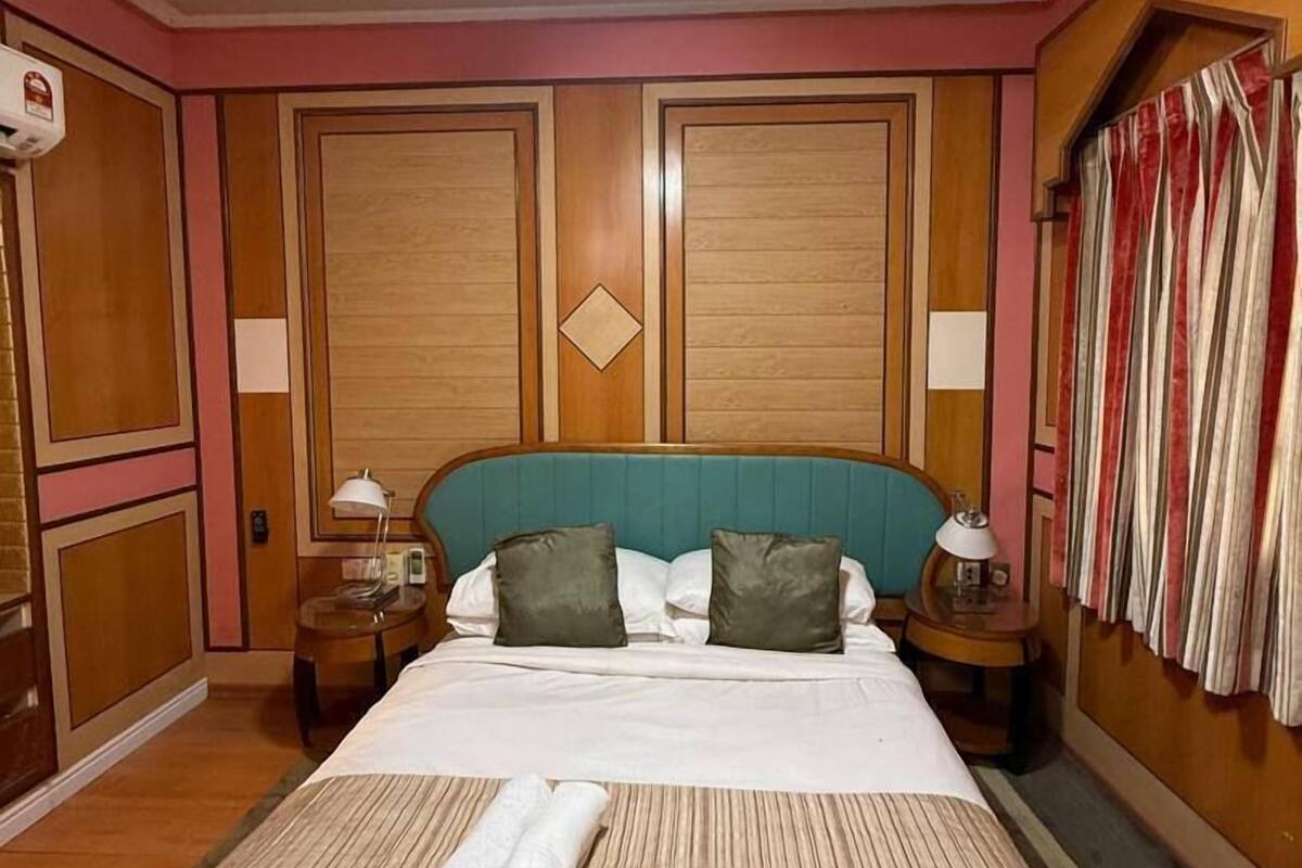 Ein Hotelzimmer mit Bett, Deckenventilator, Nachttisch, Lampe und einem Fenster mit Vorhängen.