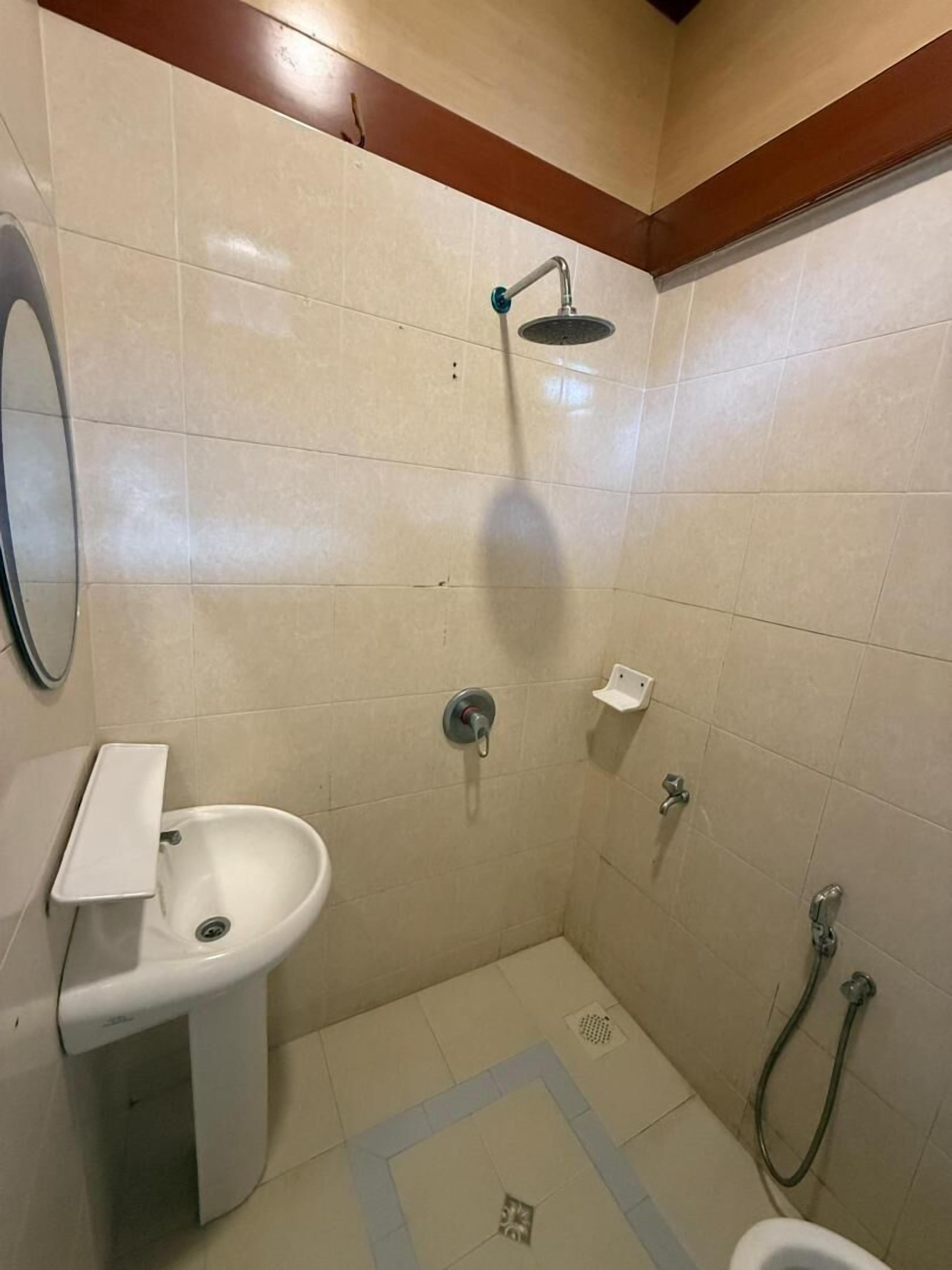 A small, tiled bathroom with a white sink, a shower, and a toilet.