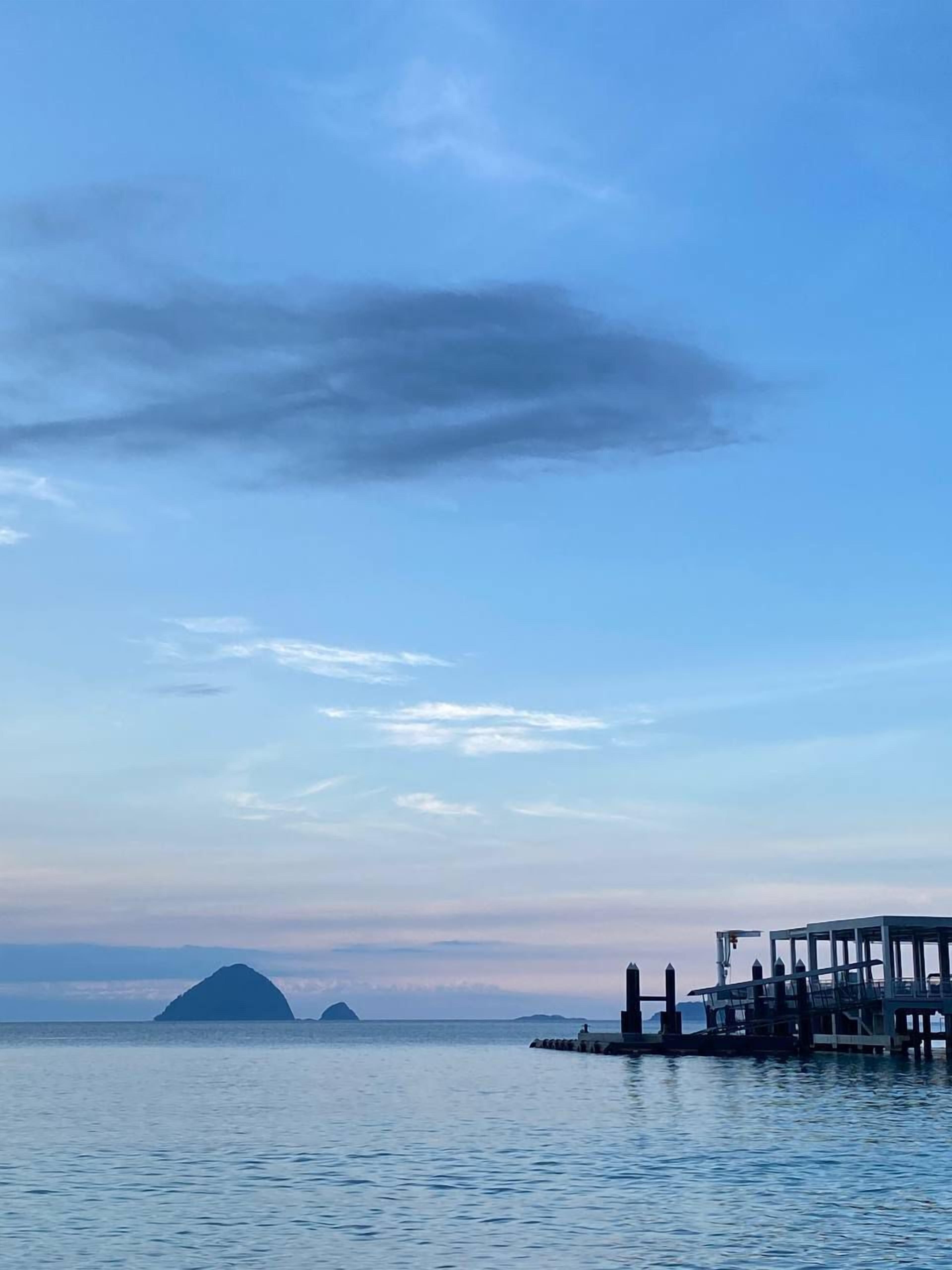 A pier extending into calm waters with a clear sky and distant landforms.