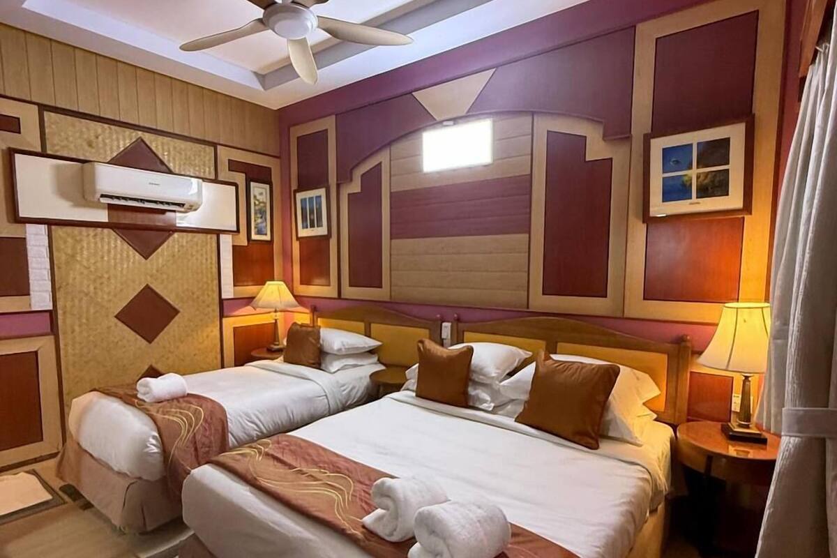 Ein Hotelzimmer mit zwei Betten, einem Deckenventilator, einer Klimaanlage und einem Nachttisch mit Lampe.