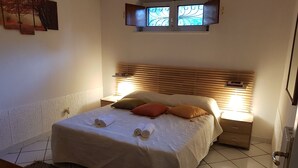 A neatly made bed with pillows, a bedside table, and a window with decorative glass. - Rent a villa 450 square meters and a chalet 60 square meters Catania (Lavinaio)