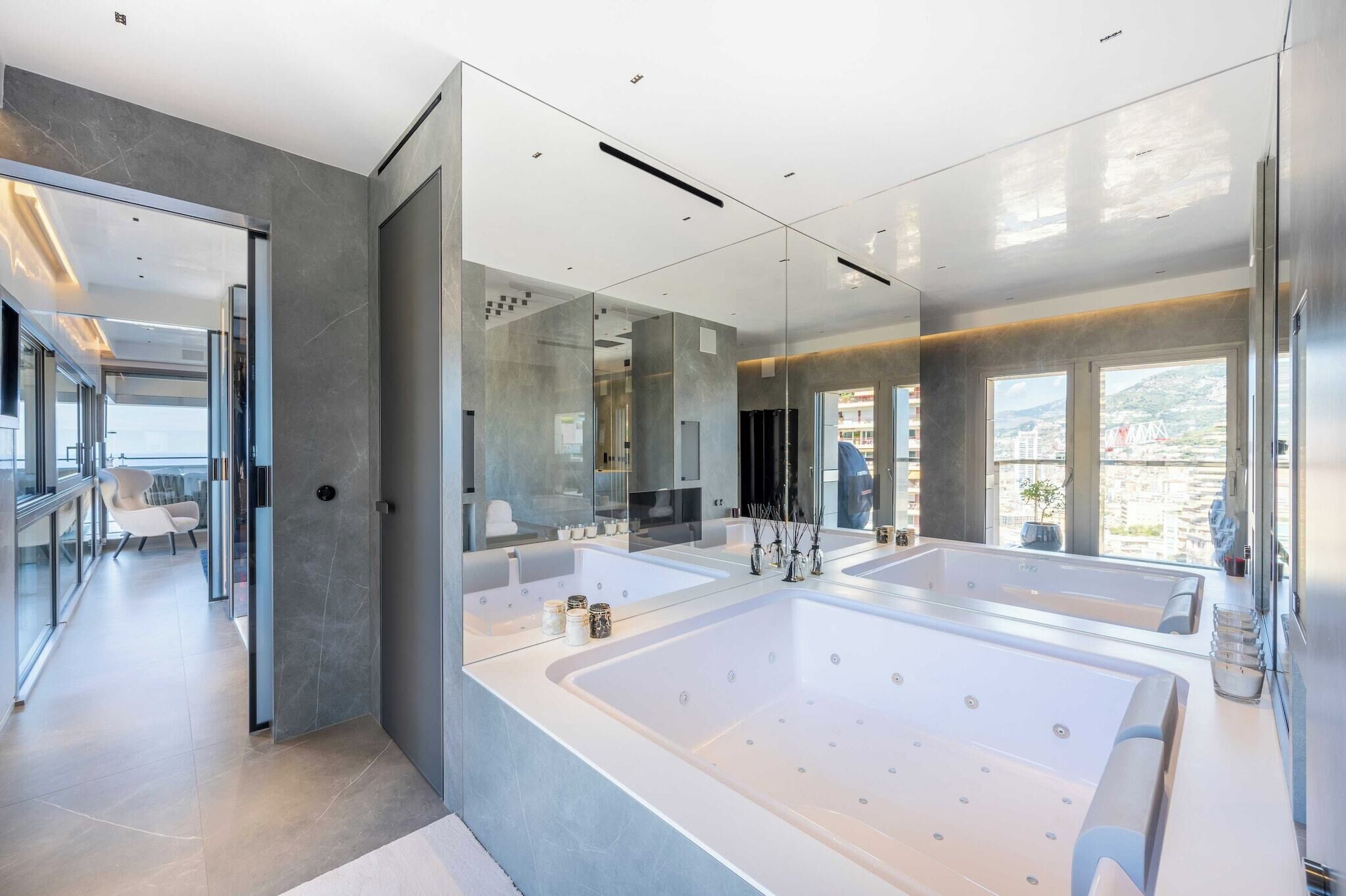 A modern bathroom with a large bathtub, a mirror, and a view of the city.