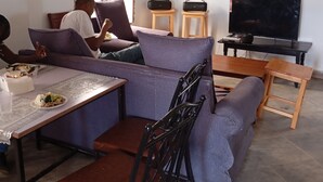 Ein Wohnzimmer mit einer Couch, Sesseln, einem Esstisch gedeckt mit Speisen, einem Fernseher und einem Fenster.