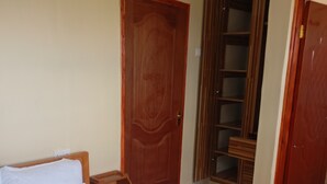 Ein ordentlich gemachtes Bett mit weißer Decke und Kissen, ein Nachttisch aus Holz mit einer Lampe und ein Holzschrank.