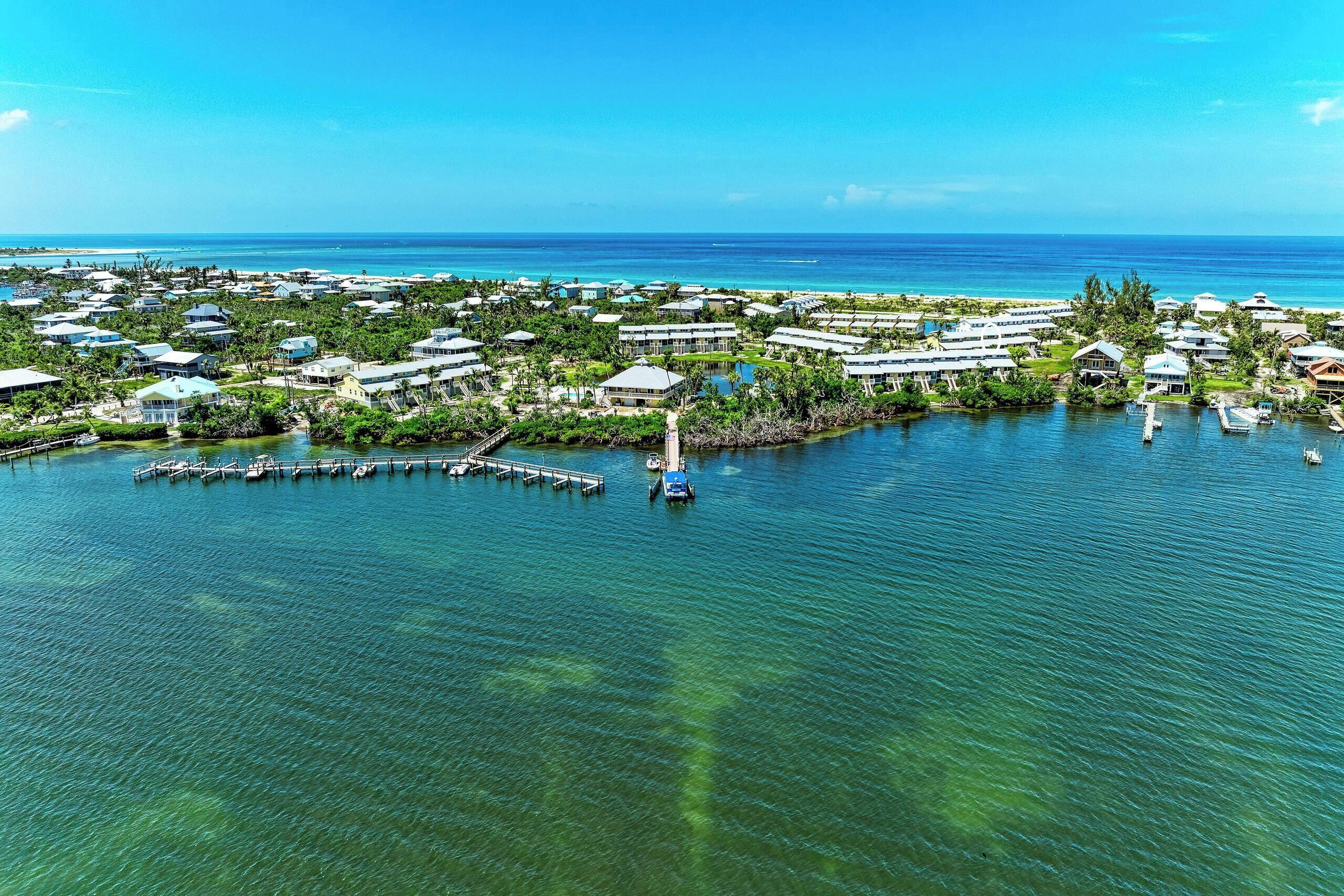 Luftaufnahme eines Küstenresorts mit mehreren Gebäuden, einem Yachthafen und klarem, blauem Wasser.