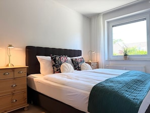 A bedroom with a bed, bedside tables, a window with a view, and a radiator.