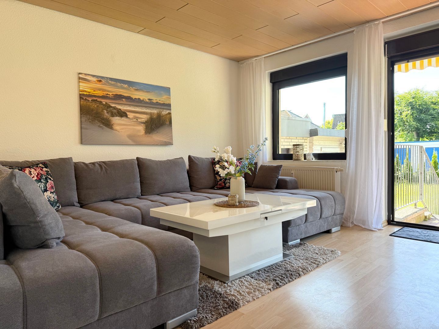Ein modernes Wohnzimmer mit einem grauen Ecksofa, einem weißen Couchtisch und einem Gemälde einer Sonnenlandschaft.