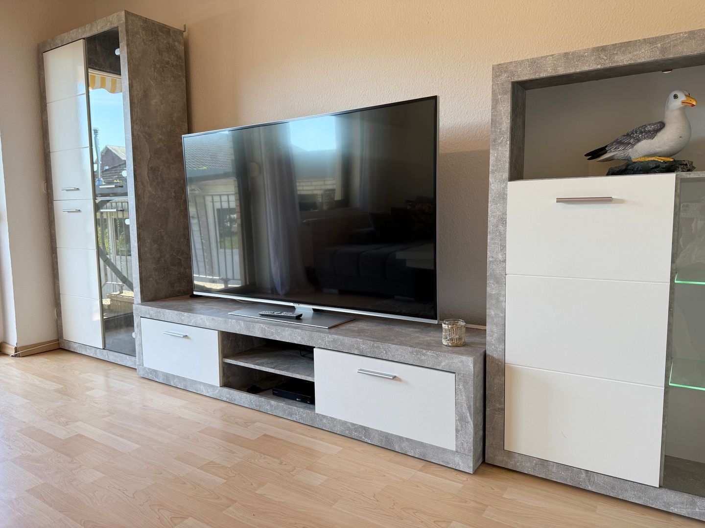 Ein modernes Wohnzimmer mit Flachbildfernseher auf einer eingebauten Konsole, einem weißen Schrank mit Glastüren und Holzboden.