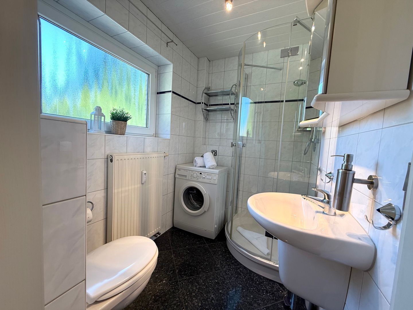 Une petite salle de bain comprenant des toilettes, un lave-linge et une douche.