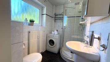 Ein kleines Badezimmer mit Toilette, Waschmaschine und Dusche.