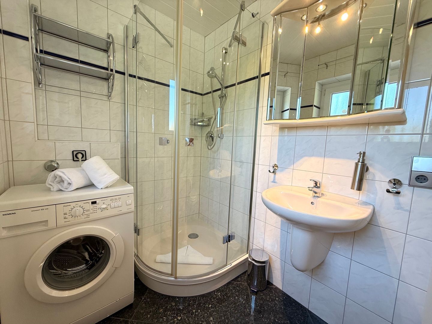 Ein modernes Badezimmer mit einer gläsernen Duschkabine, einer integrierten Waschmaschine und einem Waschbecken mit Spiegel.