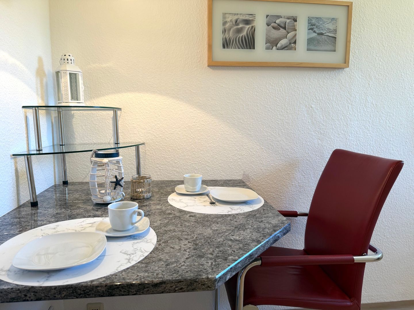 Ein Essbereich mit einem Glastisch, weißen Tellern und einem roten Stuhl.