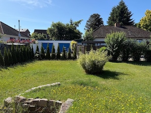 Un barrio residencial con césped, un muro de piedra y diversas especies de árboles y arbustos.
