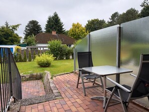A patio with a metal table and chairs, a brick pathway, and a house in the background.