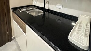A modern kitchen with a black countertop, stainless steel sink, and wooden cabinets. - 106 AL-NAJEH JRE Apartments For Rent ave (Amman)
