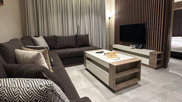 A modern living room with a dark-colored sofa, a coffee table, and a flat-screen TV. - 106 AL-NAJEH JRE Apartments For Rent ave (Amman)
