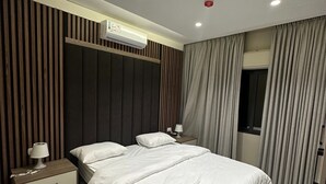 Een moderne slaapkamer met een groot bed, een nachtkastje, een lamp, een airconditioning en een raam met gordijnen.