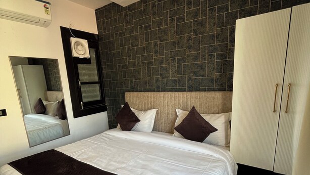Une chambre d’hôtel moderne avec un grand lit, une armoire, un miroir et un mur d’accent recouvert de carreaux foncés.