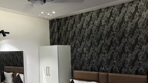 Une chambre d’hôtel moderne avec un grand lit, un ventilateur de plafond, une armoire et un papier peint à motifs.