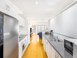 A modern kitchen with white cabinets, a stainless steel refrigerator, a granite countertop, and a yellow floor. - Cozy Hub near Food Fusion | Family Business Ideal (Sunnybank)