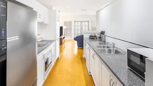 Una cocina moderna con armarios blancos, un refrigerador de acero inoxidable, una encimera de granito y piso amarillo.