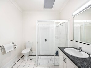 Un baño moderno con ducha de vidrio, inodoro blanco y lavamanos con encimera de granito.