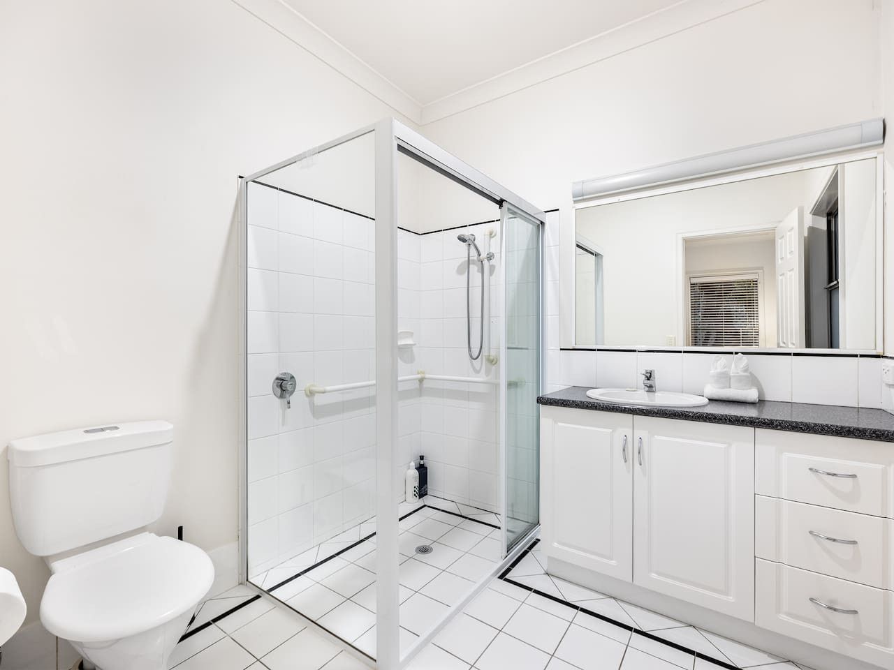 Een moderne badkamer met een douchecabine van glas, witte sanitair en een grote spiegel.