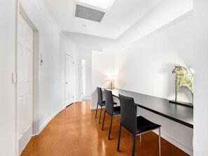 A hallway with a dining area featuring a long table and four chairs, white walls, and a ceiling vent. - Cozy Hub near Food Fusion | Family Business Ideal (Sunnybank)