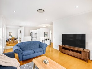 A modern living room with a blue sofa, wooden TV stand, and a flat-screen TV. - Cozy Hub near Food Fusion | Family Business Ideal (Sunnybank)