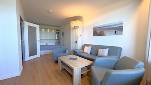 Une pièce moderne et bien éclairée, comprenant un canapé, des fauteuils, une petite table et un lit avec une tête de lit.