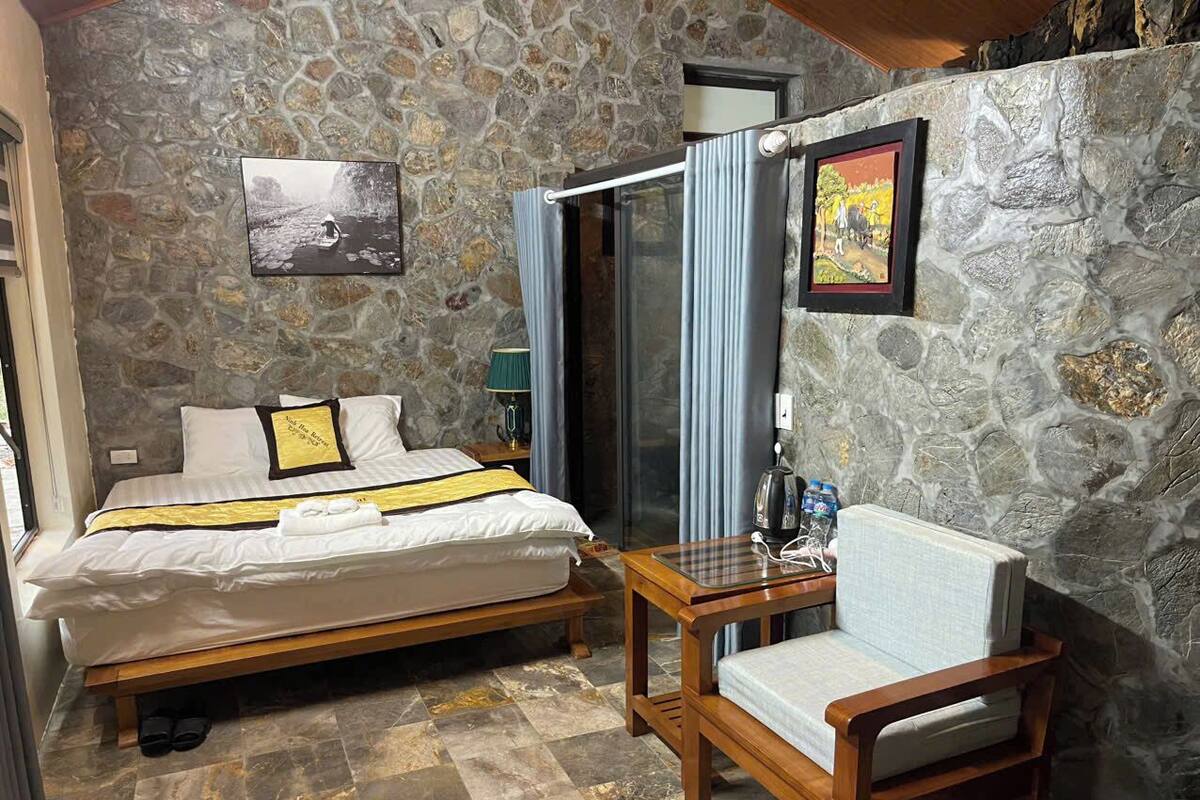 A room with a bed, a chair, a table, and a shower area.