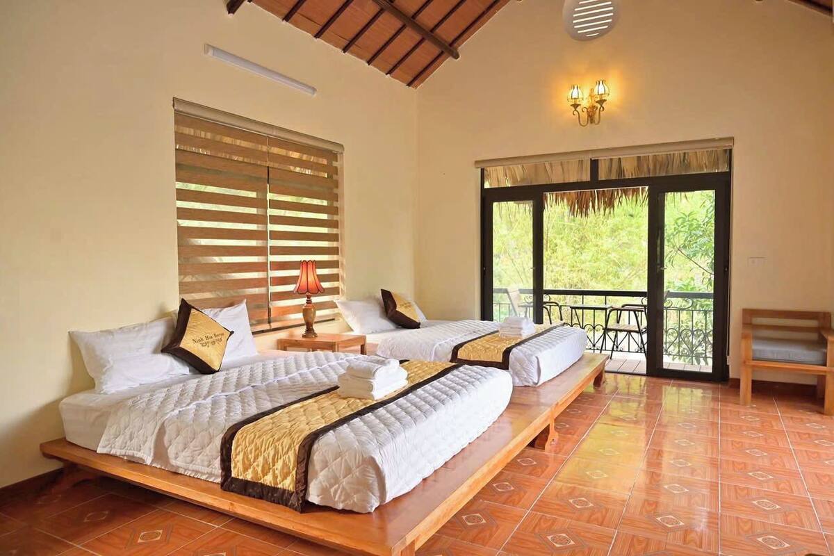 A room with two beds, a balcony, and a view of greenery.
