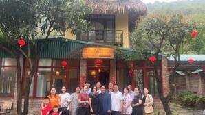 A group of people posing in front of a restaurant with a thatched roof and red lanterns. - Ninh Hoa Retreat (Tay Hoa Lu)